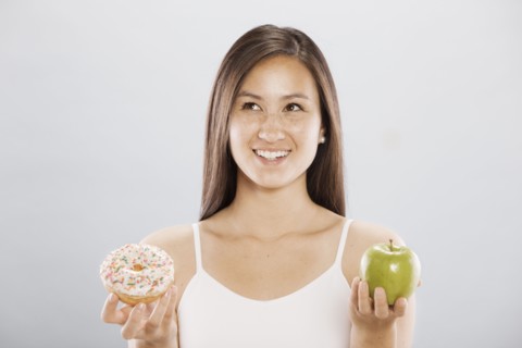 Woman holding an doughnut and an apple. Photo : FBP