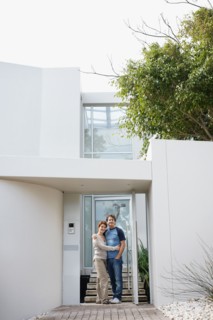 Happy couple embracing in front of their home. Photo : momentimages