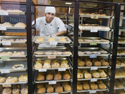 Baker standing behind trays of baked goods. Photo. Erik Isakson