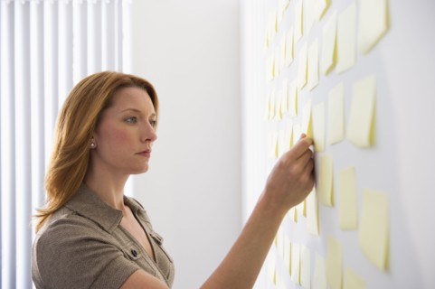 Businesswoman putting sticky note on wall.