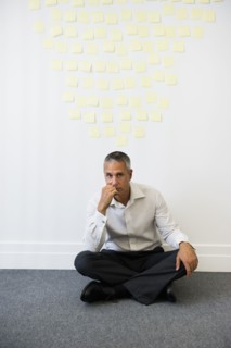 Businessman sitting behind wall covered in sticky notes.