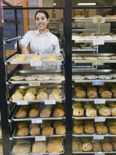 Baker standing behind trays of baked goods. Photo. Erik Isakson