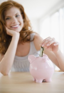 Woman putting money in piggy bank. Photo. Jamie Grill