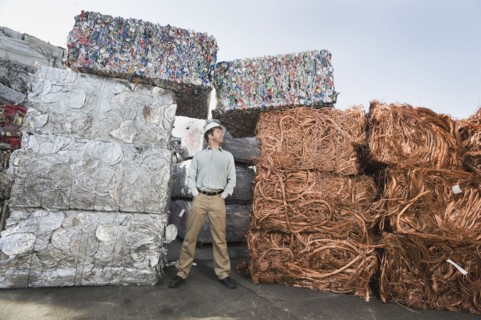 Worker standing beside stacks of recycled material.