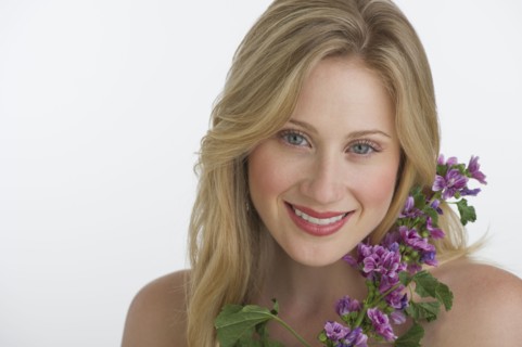 Blond woman holding purple flowers.