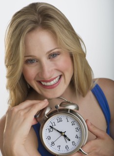 Happy blond woman holding an alarm clock.