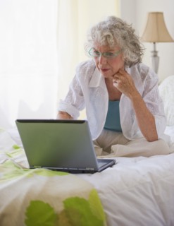 Woman looking at laptop in bedroom. Photo : Daniel Grill