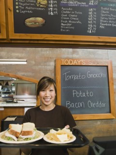 Woman holding tray of food in bakery.