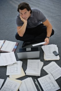 Man sitting on floor with laptop with documents around.