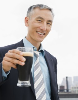 Businessman holding pint of ale and looking at camera. Photo : Jamie Grill