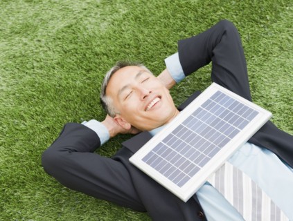 Happy businessman lying on grass with eyes closed and hands behind head and with solar panel on