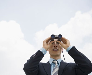 Businessman looking away through binoculars. Photo : Jamie Grill
