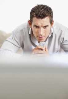 Tense man holding remote control in front of television. Photo : Momentimages