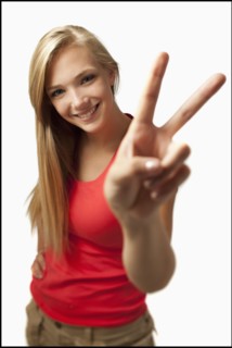 Young woman on white background showing peace sign. Photo : Mike Kemp