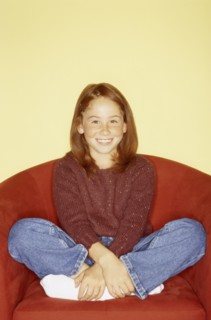 Cute young girl sitting in red chair. Photo : Fisher Litwin