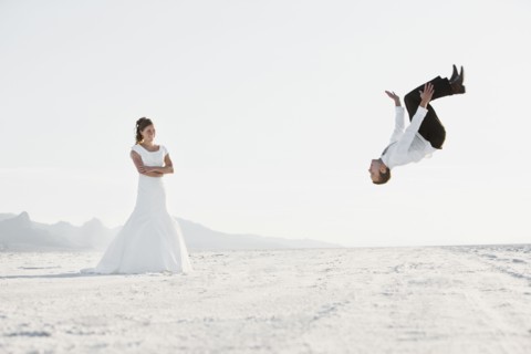 Bride watching groom performing backflip in desert. Photo : FBP