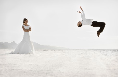 Bride watching groom performing backflip in desert. Photo : FBP