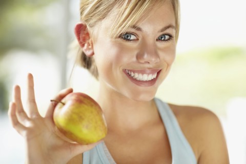 Portrait of young blonde woman holding apple. Photo : Momentimages