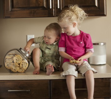 Baby boy and girl (1-3) sharing cookies on kitchen worktop. Photo : Mike Kemp