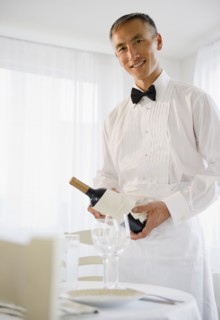 Smiling waiter holding champagne bottle and looking at camera. Photo : Jamie Grill