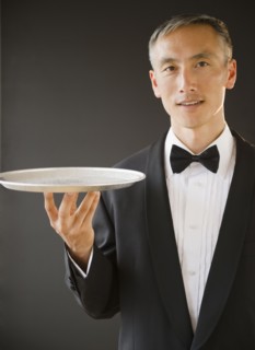 Waiter wearing bow tie and holding tray, studio shot. Photo : Jamie Grill