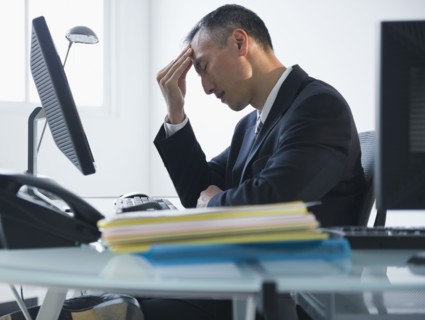 Businessman with headache sitting in office. Photo : Jamie Grill