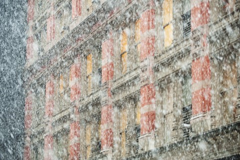 Snow falling in front of apartment building.