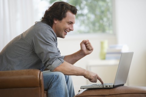 Man on armchair using laptop and laughing.
