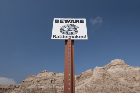 USA, South Dakota, Badlands National Park, Rattlesnake warning sign against sky, mountain in background.