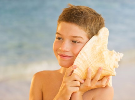 Boy (10-11) listening to sea shell on beach. Photo : Daniel Grill