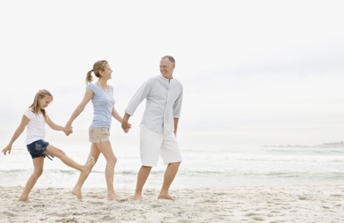 Parents with daughter (10-11) walking on beach. Photo : Momentimages