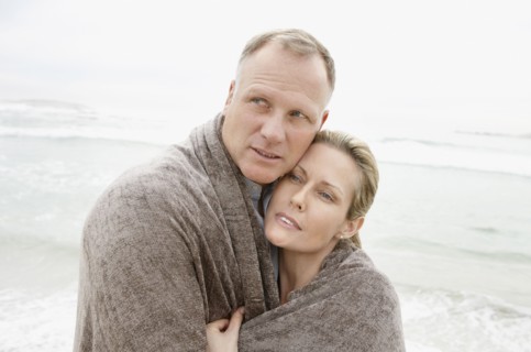 Embraced couple covered by blanket looking away on beach. Photo : Momentimages