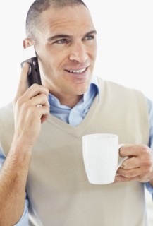 Office worker holding mobile phone in one hand and cup in another. Photo : Momentimages