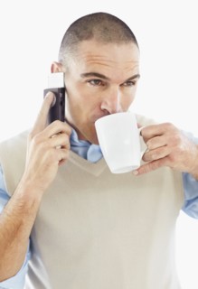 Office worker drinking while using mobile phone. Photo : Momentimages