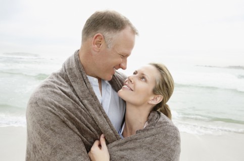 Embraced couple covered by blanket looking each other. Photo : Momentimages