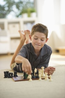 Boy (10-11) lying on floor and playing chess. Photo : Daniel Grill