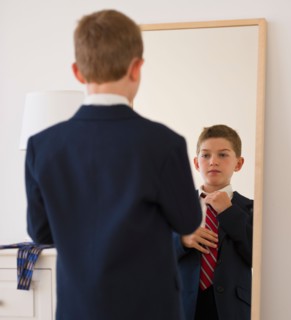 Boy (10-11) adjusting tie in front of mirror. Photo : Daniel Grill