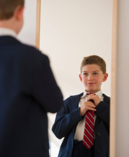 Boy (10-11) adjusting tie in front of mirror. Photo : Daniel Grill