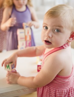 Girls (18-23 months, 4-5) playing with blocks and looking at camera. Photo : Jamie Grill