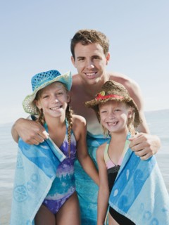 Portrait of girls (6-7,8-9) wrapped in towel on beach with their father.
