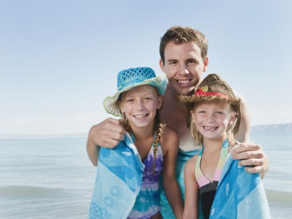 Portrait of girls (6-7,8-9) wrapped in towel on beach with their father.