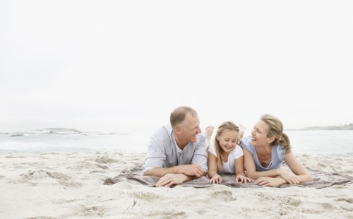 Two parents lying on beach with daughter (10-11). Photo : Momentimages
