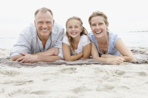 Two parents lying on beach with daughter (10-11). Photo : Momentimages