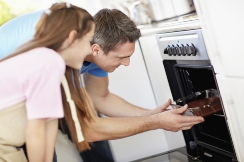 Daughter (10-11) putting cake inside of oven. Photo : Momentimages