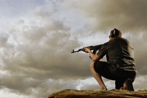 Man aiming gun on rocks. Photo : Shawn O'Connor