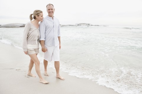 Couple holding hands and walking on empty beach. Photo : Momentimages