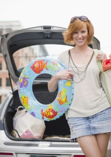 Portrait of young woman with beach gear in front of car. Photo : Jamie Grill