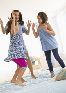 Sisters (2-3, 8-9, 12-13) jumping on bed. Photo : Daniel Grill