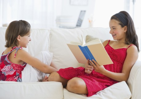 Older sister (12-13) reading book to younger (8-9). Photo : Daniel Grill
