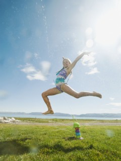 Girl (8-9) jumping over watering system.